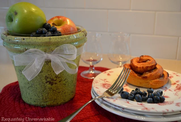 Flower pot fruit bowl filled with fruit next to a plate with fruit