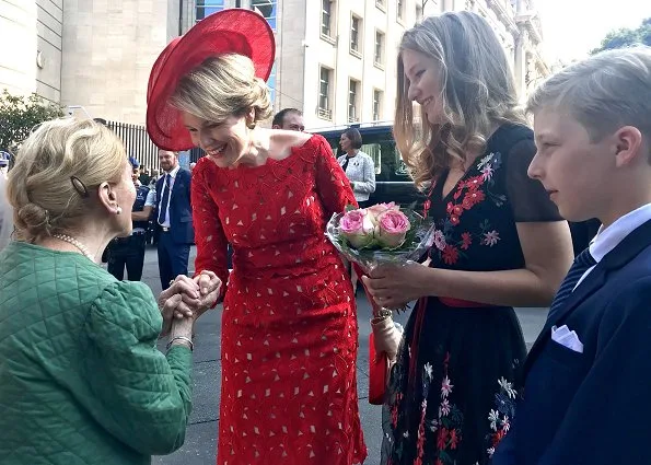 Crown Princess Elisabeth is wearing black floral print wrap midi dress. Queen Mathilde wore a red lace dress by Natan. Princess Eleonore