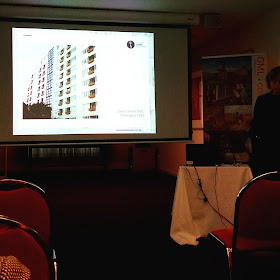Rebecca Hawcroft giving a talk in front of a slide of the modernist Dixon Street Flats in Wellington.