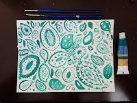 teal painted paisley pattern with 2 paintbrushes above and a paint tube