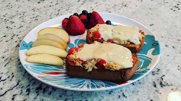 image of a dinner plate with two pieces of toast turned into mackerel melts, accompanied by some berries and apple slices