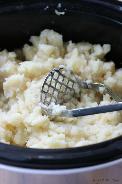 Mashed potatoes being mashed with a potato masher in a slow cooker