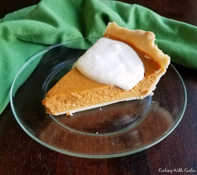 This pumpkin pie is kissed with a bit of maple flavor to heighten the warm sweet notes. Such a small change makes a big difference! slice of pie on plate with soft whipped cream on top
