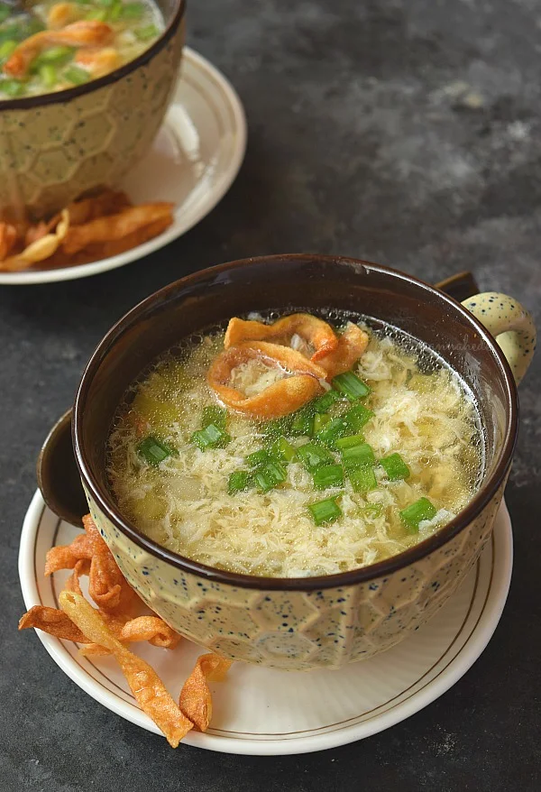 A soup bowl served with Egg drop soup topped with scallions and fried noodle