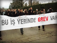 Üzerinde bu iş yerinde grev var yazılı bir pankart taşıyan grevdeki yürüyen işçiler