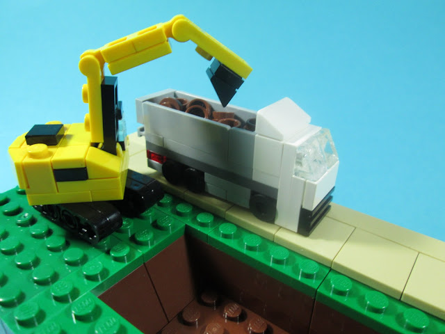 MOC LEGO - uma escavação a decorrer onde se vê uma escavadora e um camião para carregar a terra. Cena LEGO construída em micro escala.