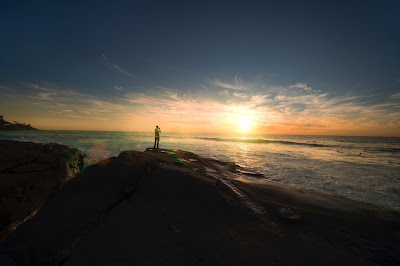 Man standing on cliff overlooking the ocean and sunset