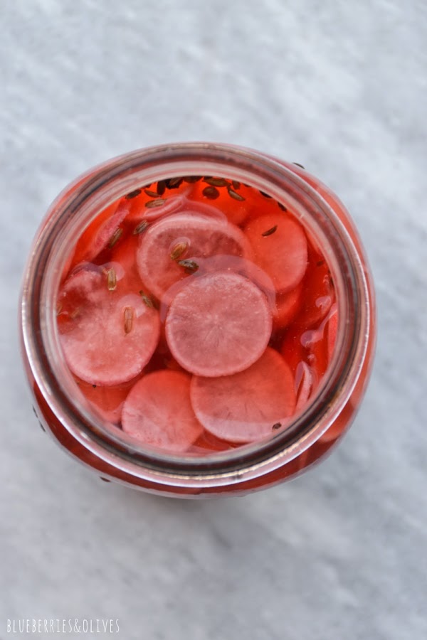 VISTA CENITAL TARRO CON RABANOS MARINADOS, SEMILLAS DE COMINO Y ALCARAVEA, PIMIENTA ROJA, FONDO MÁRMOL BLANCO