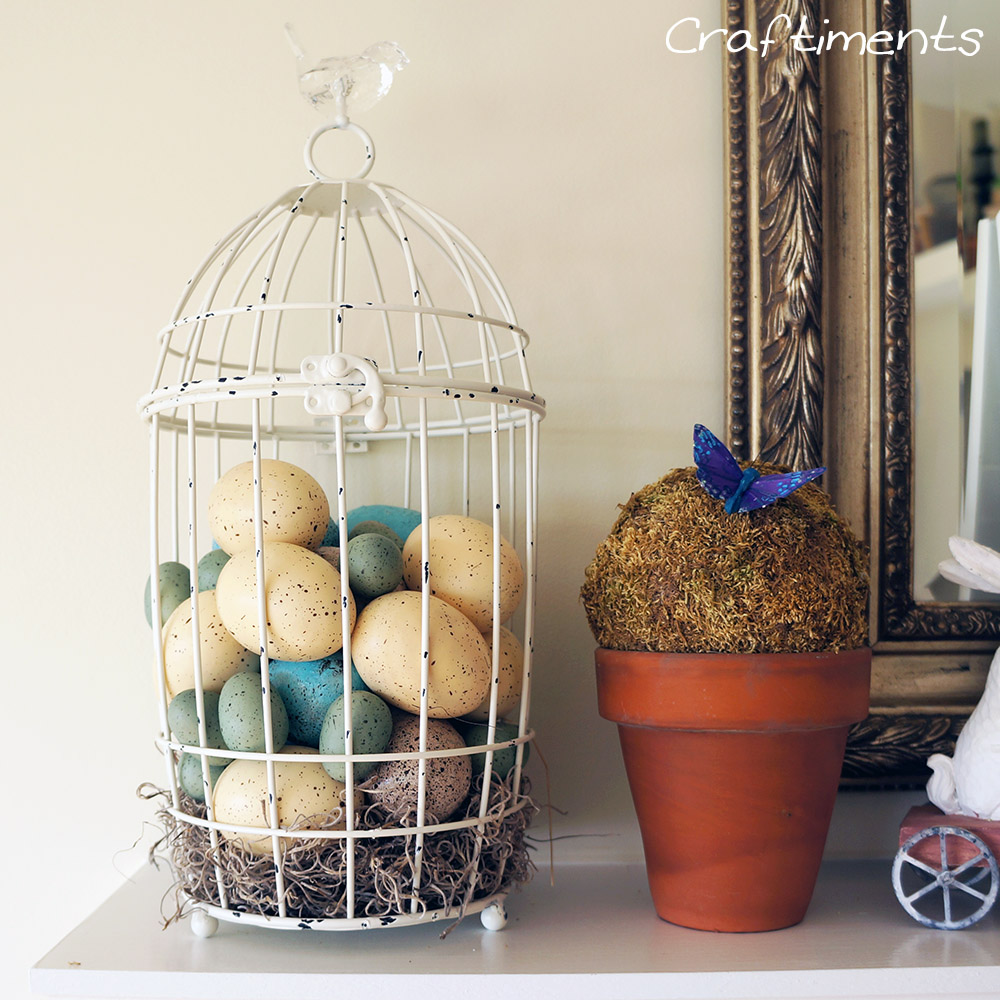 Craftiments:  Bird cage filled with faux eggs and a simple moss topiary in a terracotta flowerpot