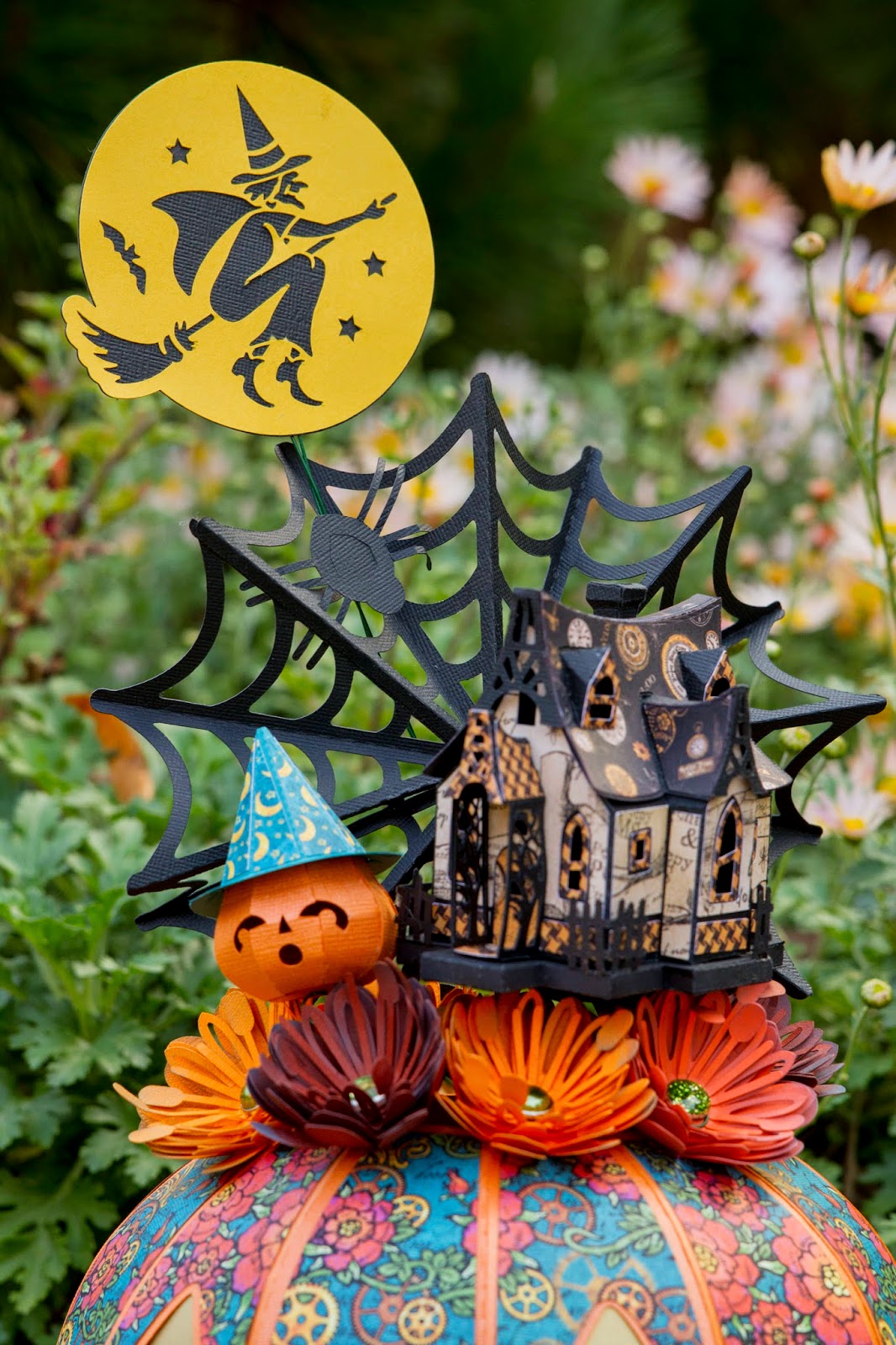 Close up of top of pumpkin showing scene of a small pumpkin, witch house, spiderweb and flowers