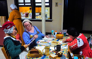 Scribes Working and Sharing Information 3 women in medieval style clothing sit at a table painting and talking