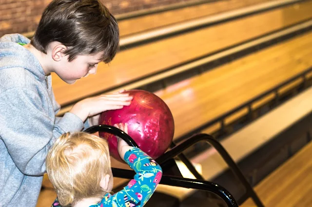 An older child helping a younger child position the bowling ball and enjoy the party
