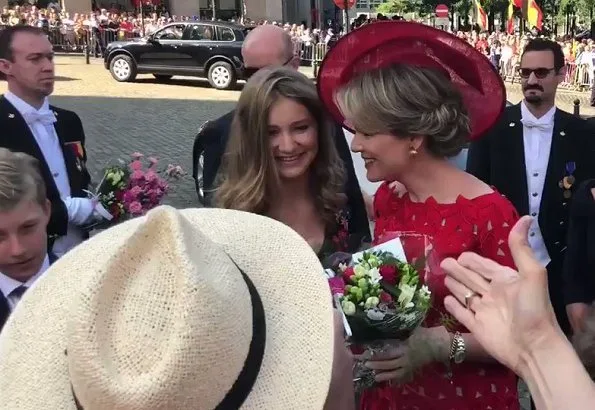 Crown Princess Elisabeth is wearing black floral print wrap midi dress. Queen Mathilde wore a red lace dress by Natan. Princess Eleonore