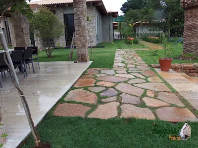 Execução do caminho no jardim com pedra Goiás tipo cacão com juntas de grama, dos revestimentos de pedra na fachada da residência em Piracaia-SP com execução do paisagismo e o gramado com grama esmeralda.