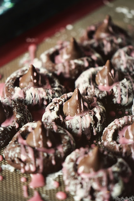 ten chocolate thumbprint cookies on a baking sheet with Hershey kiss candies and a pink glaze