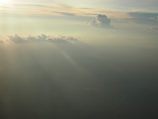 view of a darkening sky, from above clouds, a mist covers most of it, in foreground sunlight comes over a line of clouds, like a waterfall of light