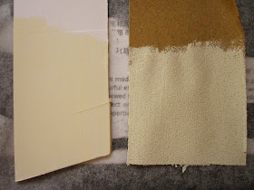 A sample iece of cardboard and a sample piece of sandpaper, both painted with cream paint, laid out to dry.