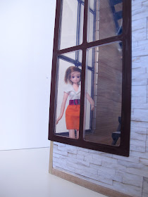 A doll looking through the corner window of the modern Lori Loft to Love dolls' house.