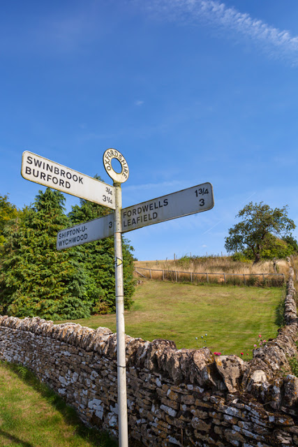 Cotswold stone wall and Cotswold signpost under a blue sky by Martyn Ferry Photography