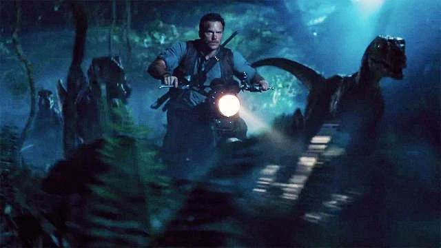 Actor Chris Platt aboard a Triumph Scrambler speeds through a jungle flanked by his Velociraptors