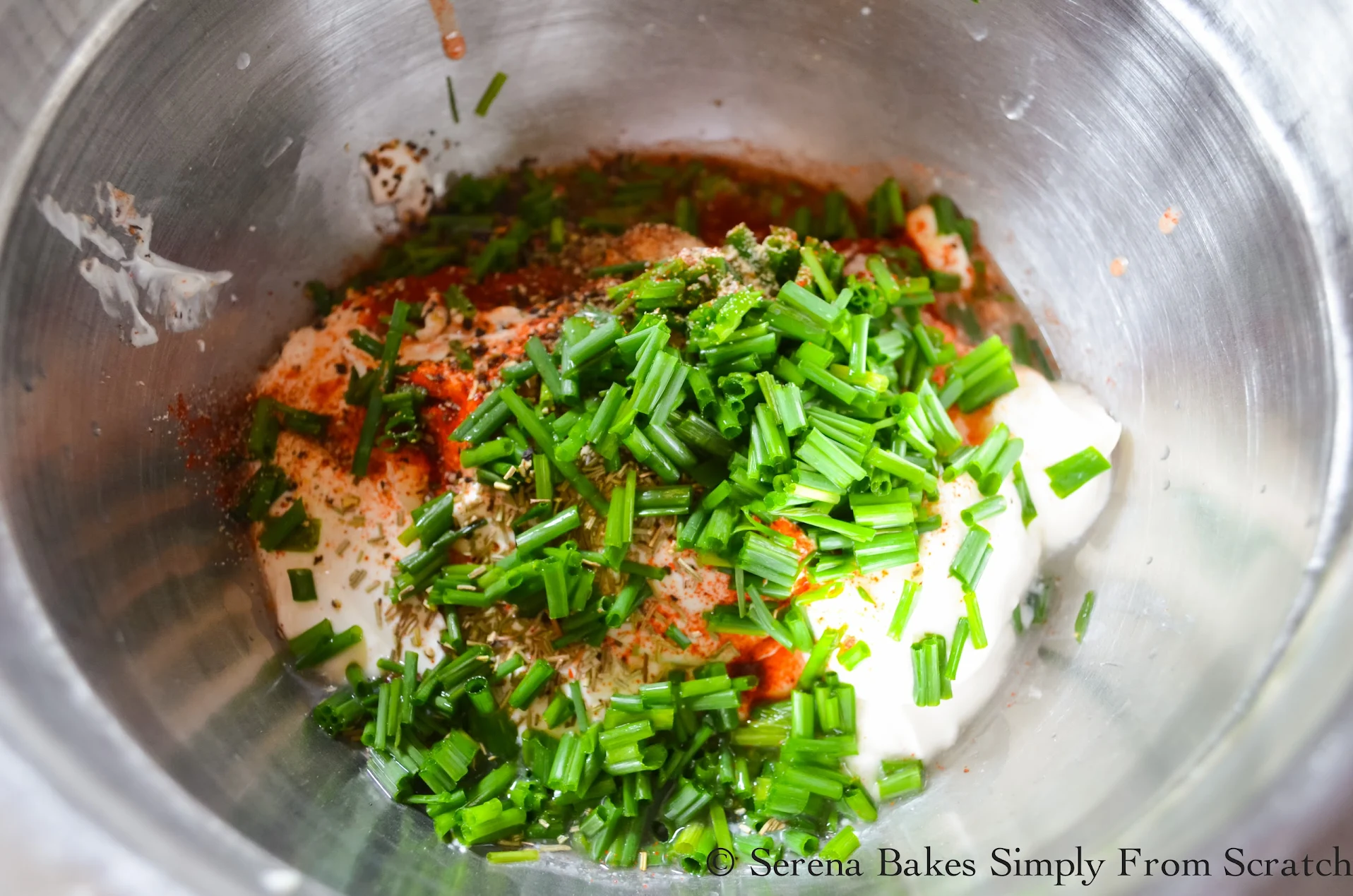A stainless steel bowl with mayonnaise, sour cream, greek yogurt, balsamic vinegar, rosemary, garlic, smoked paprika, salt and chives.