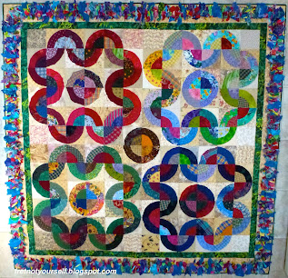 Thirty-six bullseye blocks are arranged by color into four 'flower petal' shapes on a quilt with a Texas Mink fringe border.