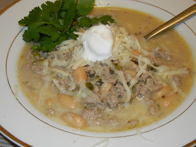 close up photo of soup in a bowl with cheese and sour cream on top with parsley as garnish and a spoon to the left 