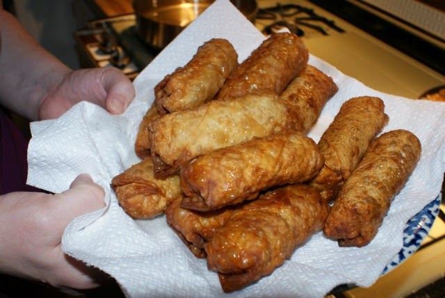 A person's hands holding a paper towel-lined plate filled with egg rolls.