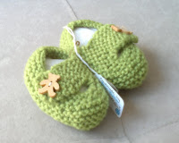 A pair of  green knitted baby shoes, each with a wooden teddy-bear-shaped button.