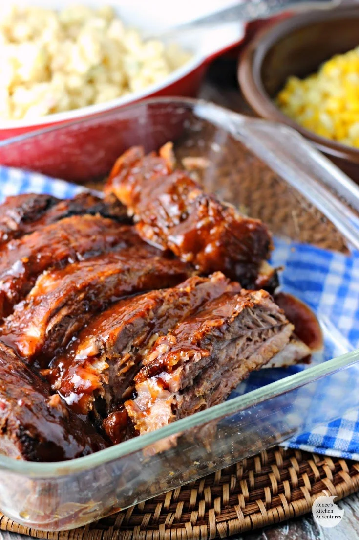 Fall-Off-The-Bone Slow Cooker Ribs by Renee's Kitchen Adventures ready to serve in clear serving dish with sides in the background