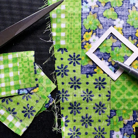 Retro cheater fabric in green, white and blue with a square template and pen on top of it, and scissors and cut out squares of fabric next to it.