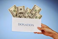 Photo of a hand holding an envelope labeled "DONATION", stuffed with dollar bills