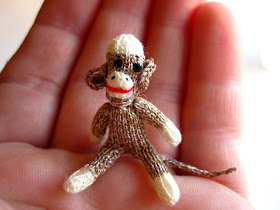 1/12th scale hand knitted sock monkey sitting on a hand