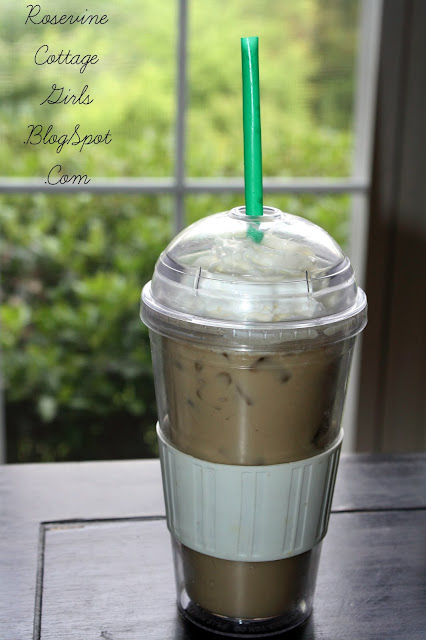 Plastic glass with iced coffee with ice cubes on a dark table with plants in the background outside of window. This is a recipe for iced coffee by rose vine cottage girls dot com