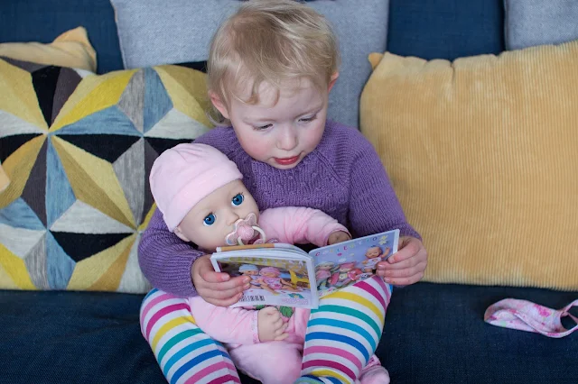 A toddler reading to Baby Annabell