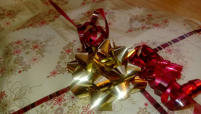 A close up of a shiny gold bow and red ribbon on top of a wrapped gift.