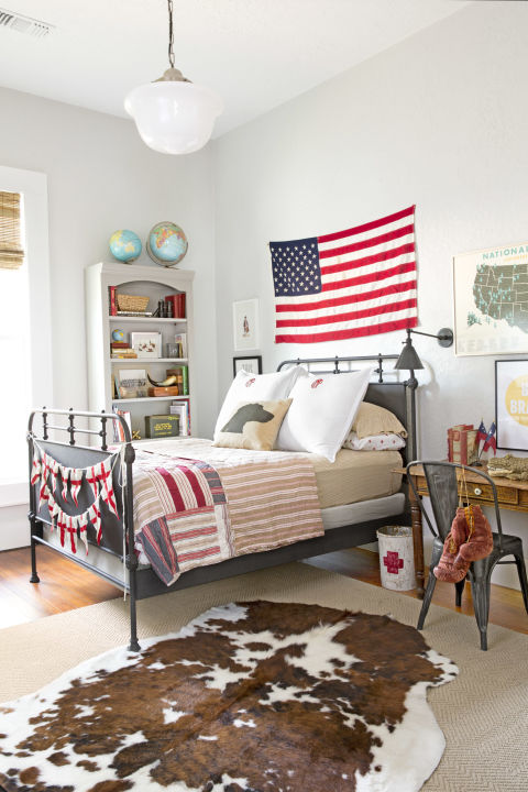 Patriotic bedroom decor in a boys room of charming cottage in Texas with interior design by Holly Mathis. American flag ung over vintage bed, cowhide rug, and French cafe chair work magic in the farmhouse style mix. #bedroom #patriotic #farmhousestyle #cottage #decorating #americana