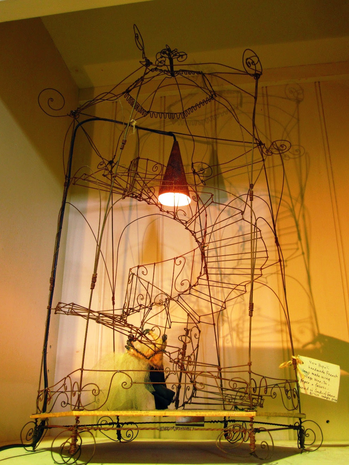 Vintage wire birdcage-shaped sculpture with wire spiral staircase and fabric doll, used as the basis for a lamp.