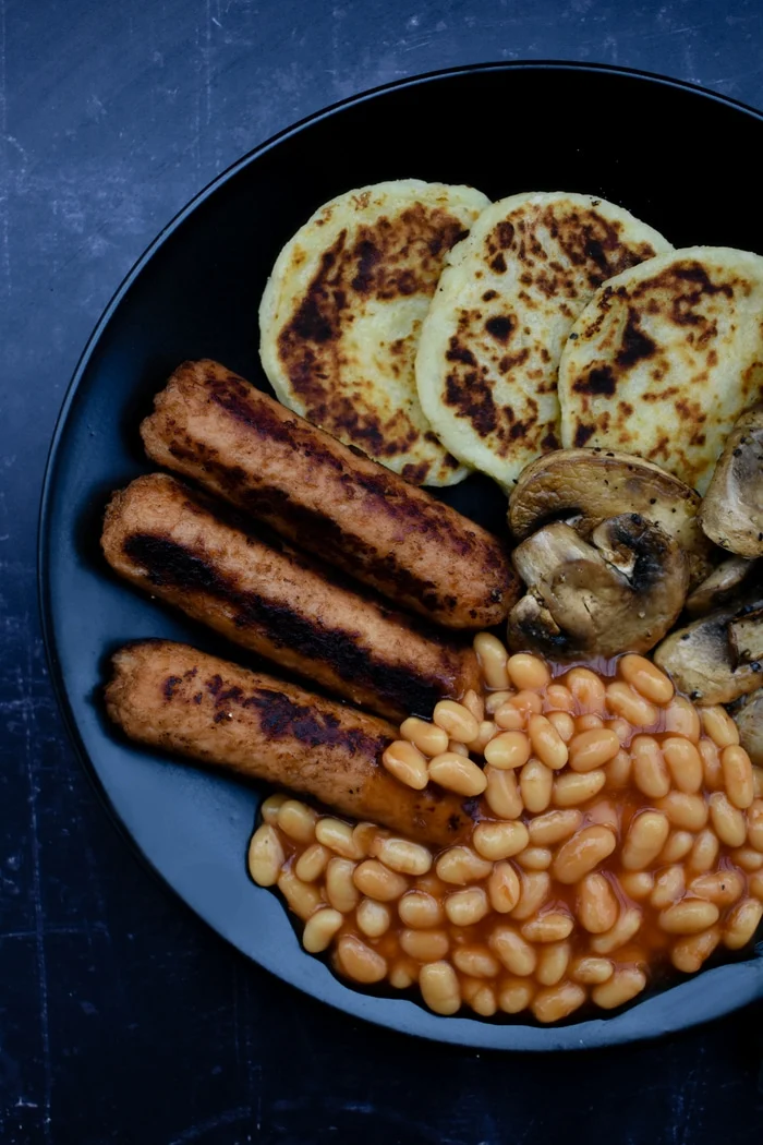 vegan cooked breakfast on a black plate including potato scones, mushrooms, baked beans and vegan sausages