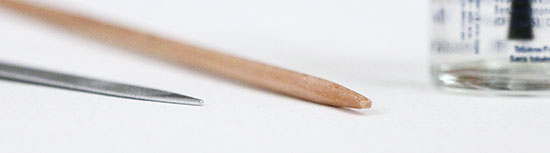 Close-up of splintered tip on a wooden knitting needle, next to nail file and polish.