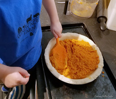 kid spreading mashed carrot filling into prepared pie crust