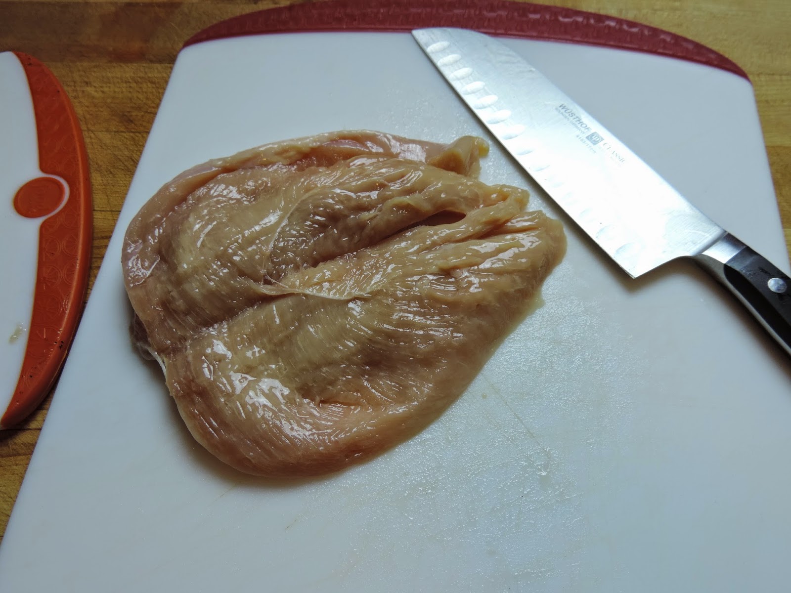 The chicken breast being cut into two cutlets. 
