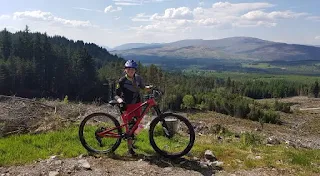 girl mountain biking with hiklls in background and trees 
