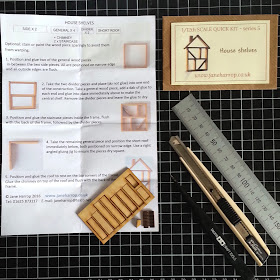 Pieces of a one-twelfth scale house shelves kit and instruction sheet, arranged on a cutting board with a ruler, cutting knife and tweezers.