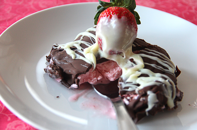 One chocolate covered strawberry klondike bar cut into exposing the strawberry ice cream inside.