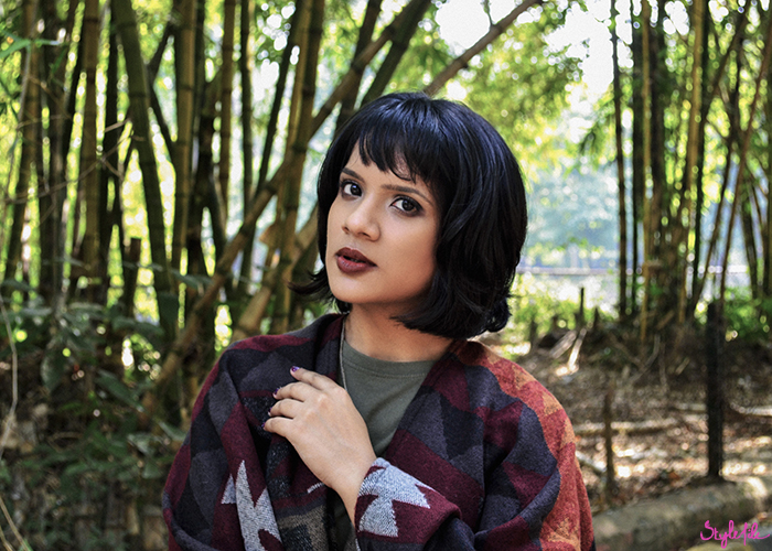 Image of a girl wearing an autumn winter outfit of a navajo print poncho coat, leather panel black jeans, black booties, plum copper eye makeup and a dark brown lip