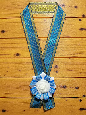 Blue graduation lei with rosette centerpiece and brocade lei Combination of blue and white satin ribbons for the rosette centerpiece coupled with blue and gold jacquard or brocade trimming