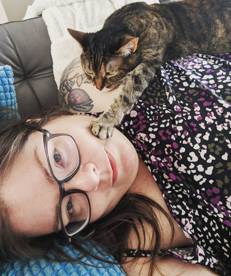 image of me lying on the couch; Sophie the Torbie Cat is lying on top of me with her paw on my cheek