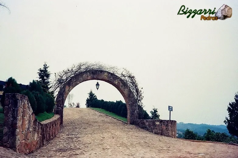 Construção do calçamento com pedra na entrada da residência em Mairiporã-SP com os muros de pedra rústica e o arco de pedra rústica com as primaveras plantadas.