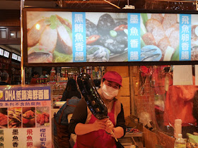 woman holding a large fake Cuttlefish Sausage